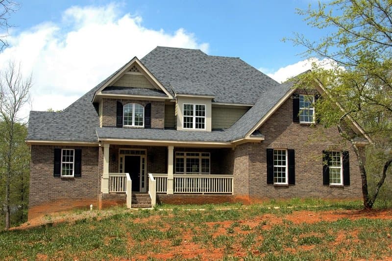 A two-story brick home with a gray architectural shingle roof and a covered front porch