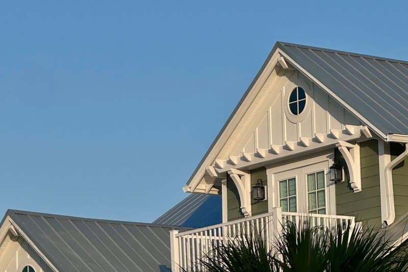 A coastal home with a standing-seam metal roof and a palm tree in warm evening light